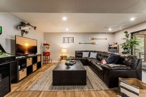 Ein modernes Wohnzimmer mit einem Ledersofa, einem Couchtisch, einem Fernseher und einem Spieltisch.