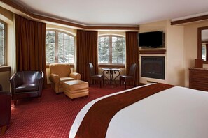 Habitación de hotel con una cama grande, chimenea, televisión y zona de estar con mesa y sillas.