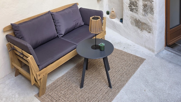 A room with a wooden sofa, a small round table, a wall-mounted light fixture, and a stone wall.