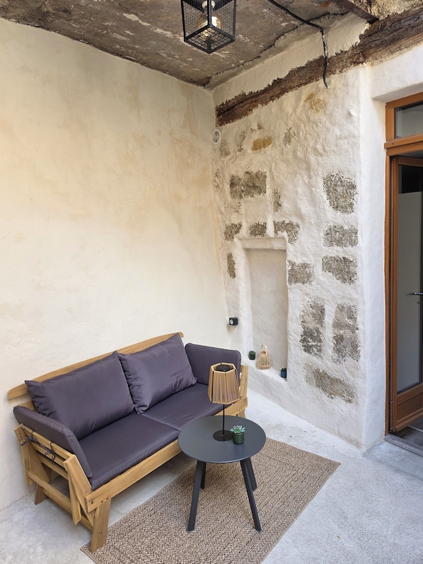 A room with a wooden sofa, a small round table, a wall-mounted light fixture, and a stone wall.