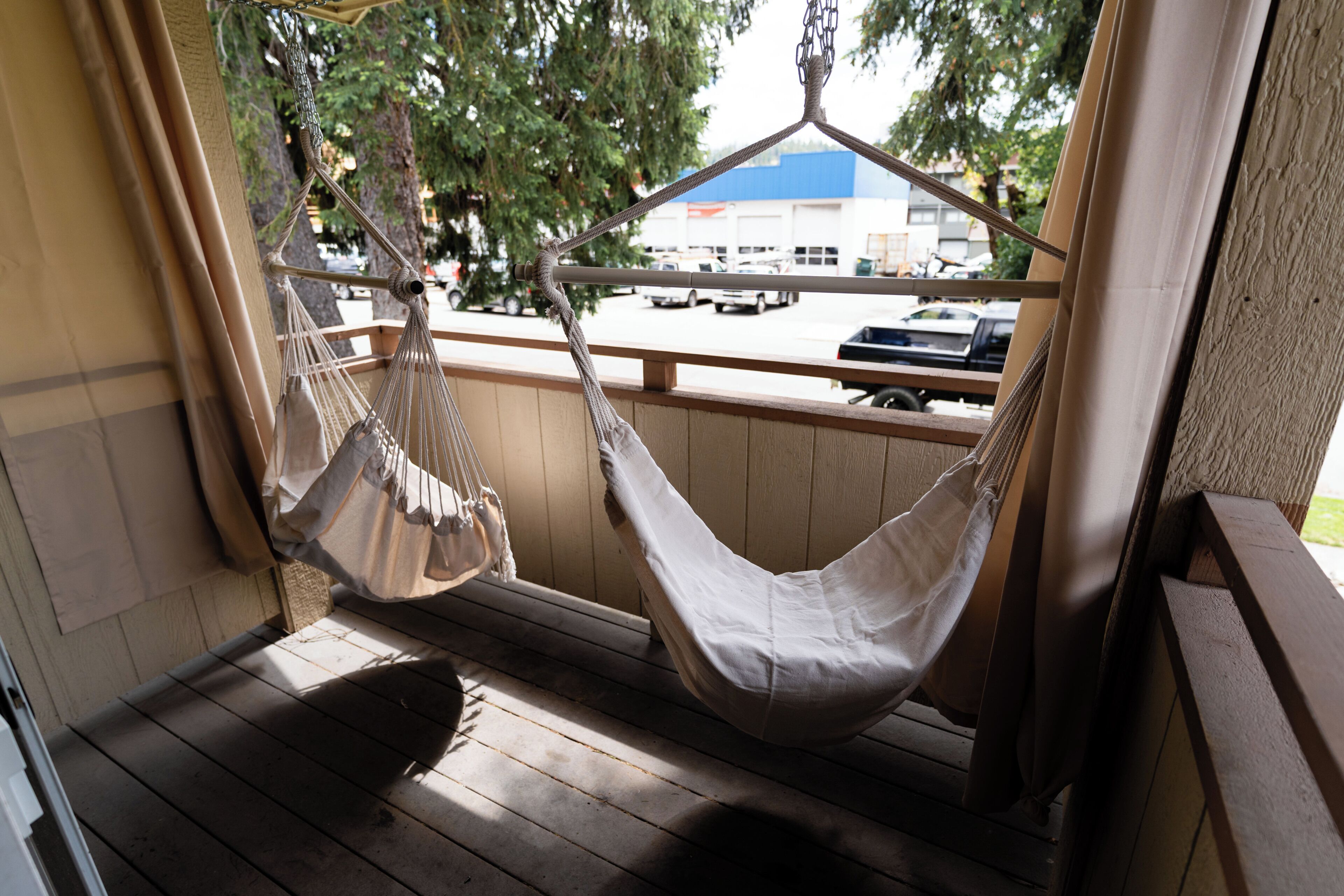 A hammock on a wooden porch with a view of a parking lot and buildings.