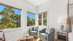 Ein Zimmer mit zwei Sesseln, einem kleinen Tisch und einer Lampe. Große Fenster bieten Blick auf Bäume.