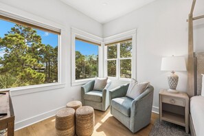 Ein Zimmer mit zwei Sesseln, einem kleinen Tisch und einer Lampe. Große Fenster bieten Blick auf Bäume.