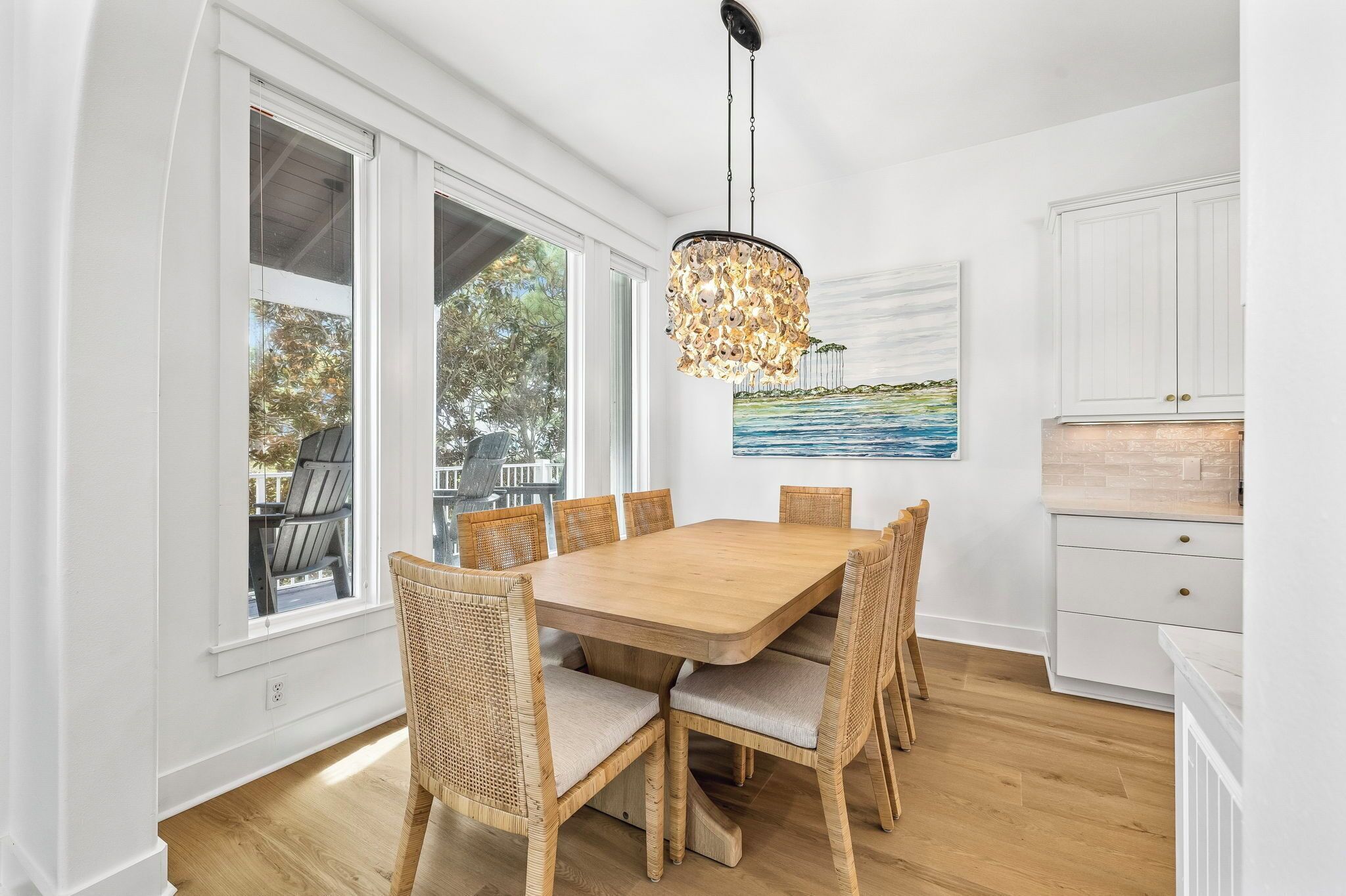 A dining area with a wooden table and wicker chairs, large windows, and a hanging light fixture.