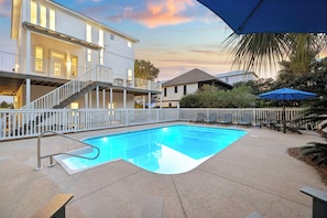 Ein Pool mit weißem Zaun, eine überdachte Terrasse und ein mehrstöckiges Gebäude im Hintergrund.