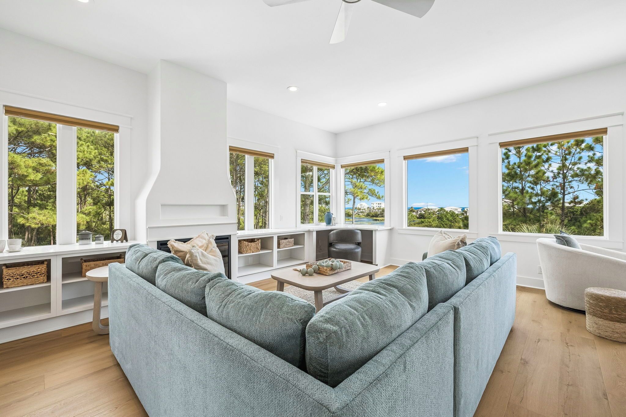 A modern living room with a sectional sofa, a fireplace, and large windows offering a view of trees and buildings.