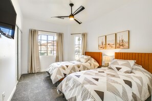 A hotel room with two beds, a ceiling fan, a window with curtains, and desert-themed wall art.