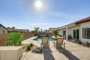 A backyard with a swimming pool, two lounge chairs, and a patio area.
