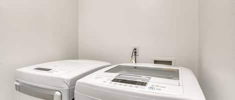 Two white laundry machines in a corner with a plain wall.