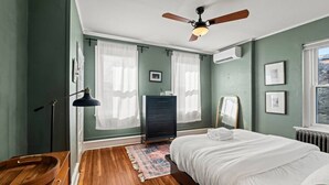 A bedroom with a bed, a dresser, a mirror, a ceiling fan, and a window with curtains. - Charming 3BR East Falls Home with Fenced Yard & Office (Philadelphia)