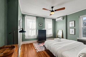 Um quarto com cama, penteadeira, espelho, ventilador de teto e janela com cortinas.