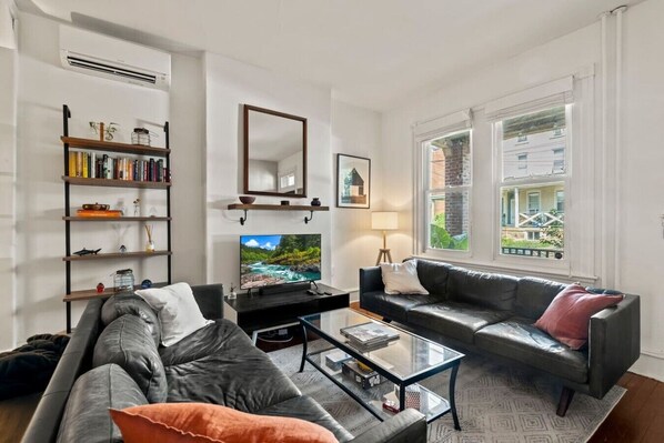 A living room with a sofa, a coffee table, a TV, a bookshelf, and a window with a view.