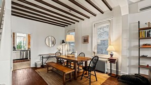 A dining area with a wooden table, chairs, and a bench. There is a radiator under a window, a lamp on a side table, and a bookshelf to the right. - Charming 3BR East Falls Home with Fenced Yard & Office (Philadelphia)
