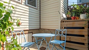 A corner patio with a round table and two chairs, a wooden fence, and potted plants. - Charming 3BR East Falls Home with Fenced Yard & Office (Philadelphia)