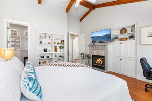 Ein Schlafzimmer mit einem großen Bett, einem Kamin, einem darüber montierten Fernseher und einem Bücherregal voller verschiedener Gegenstände.