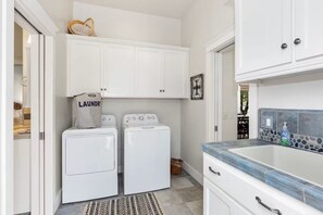 A laundry area with two washing machines, a drying rack, and a sink with a stone backsplash. - Riverfront Paradise at RedRock Villa (Three Rivers)