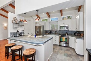A modern kitchen with white cabinetry, a central island with stools, stainless steel appliances, and pendant lighting. - Riverfront Paradise at RedRock Villa (Three Rivers)