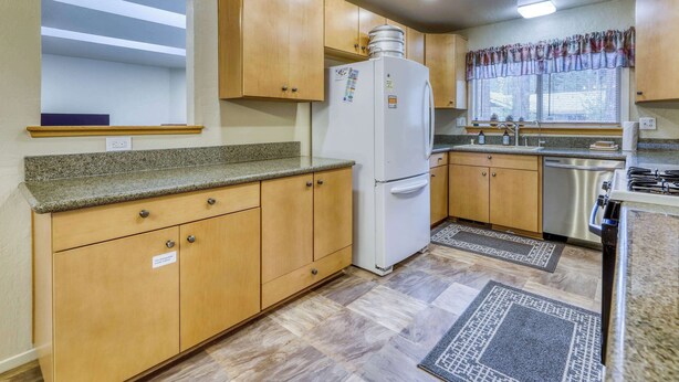 A compact kitchen with wooden cabinets, a white refrigerator, a stainless steel sink, and a stove. - Tahoe Town & Lake Retreat - Near Tahoe Keys (South Lake Tahoe)