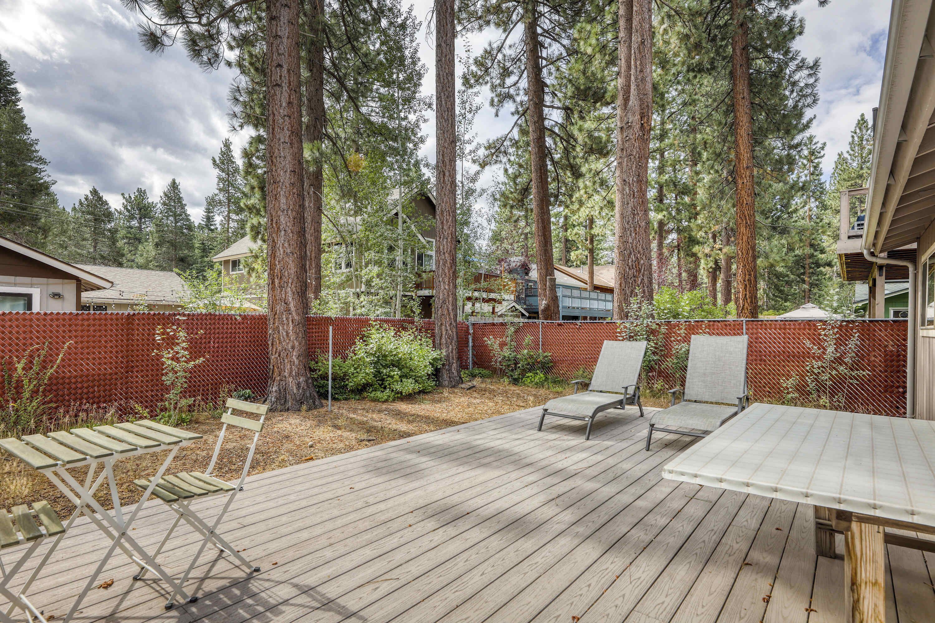 A deck with outdoor furniture, surrounded by a wooden deck and a red fence, with tall trees in the background.