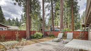 A deck with outdoor furniture, surrounded by a wooden deck and a red fence, with tall trees in the background. - Tahoe Town & Lake Retreat - Near Tahoe Keys (South Lake Tahoe)