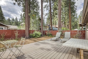 A deck with outdoor furniture, surrounded by a wooden deck and a red fence, with tall trees in the background. - Tahoe Town & Lake Retreat - Near Tahoe Keys (South Lake Tahoe)