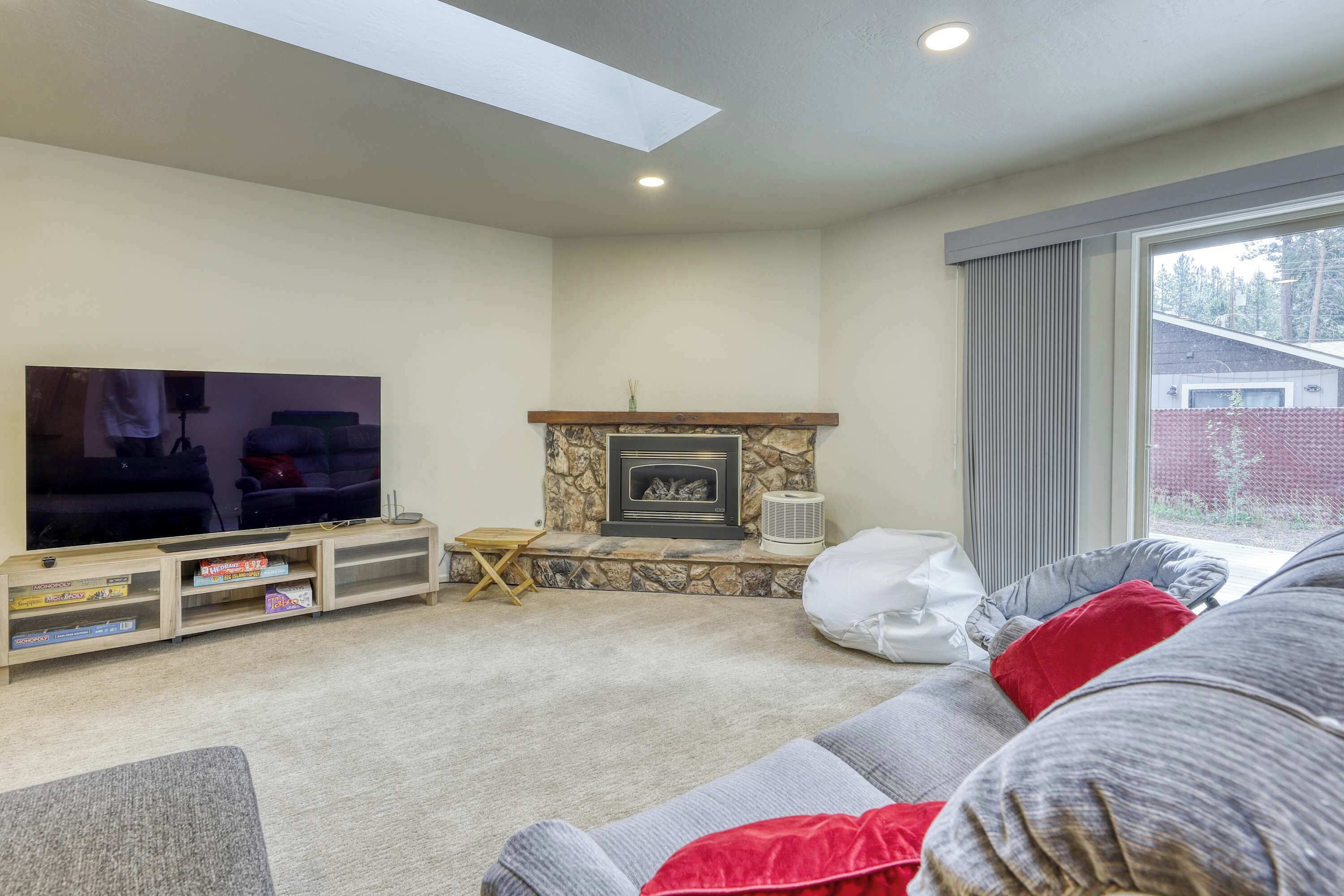 A living room with a flat-screen TV, a stone fireplace, a sofa, and a window with a view of trees.