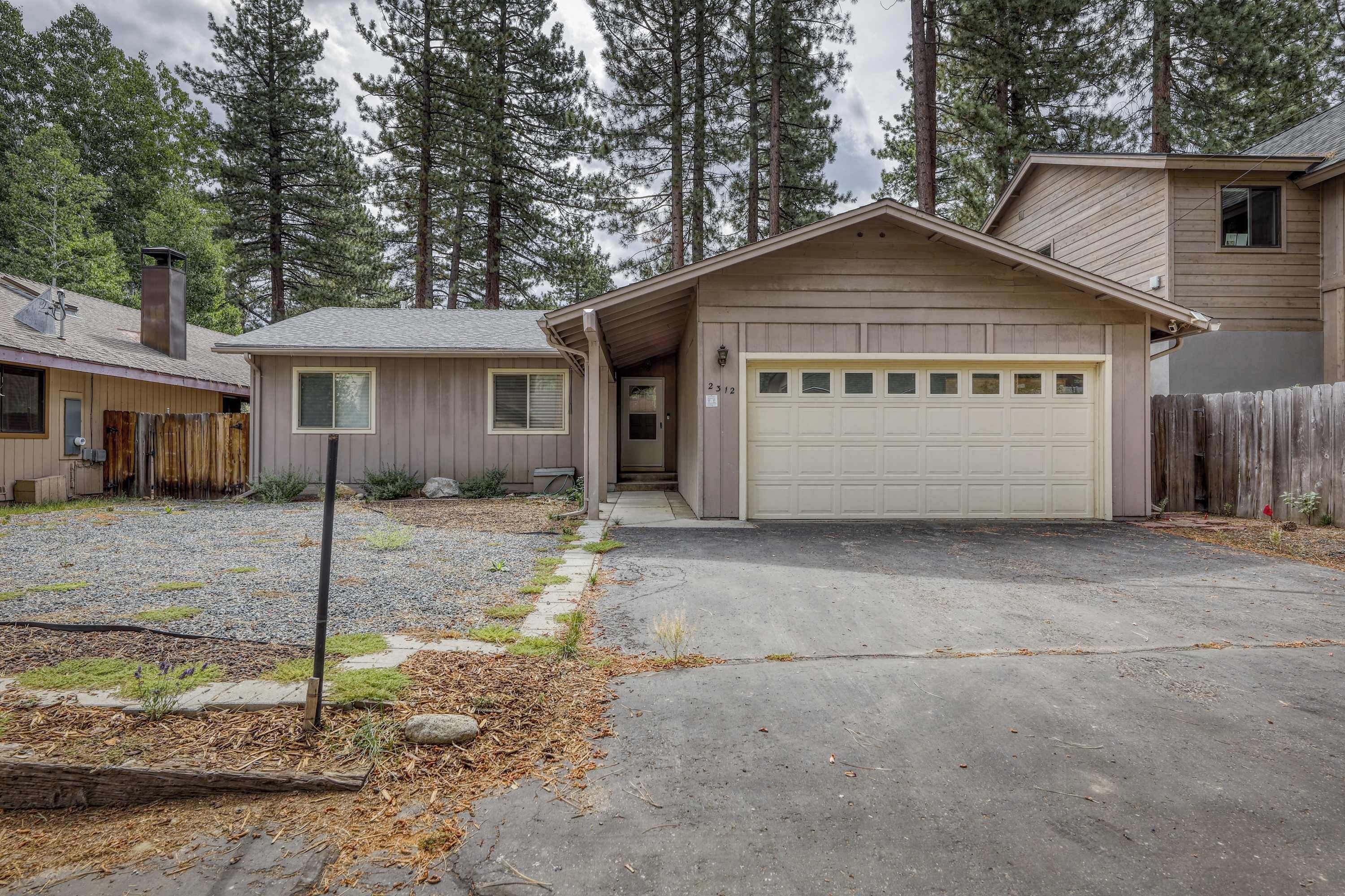 A single-story house with a garage, a front yard with gravel and small plants, and a wooden fence.
