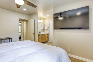 Une chambre à coucher avec un lit, un bureau, une salle de bain avec un miroir et un téléviseur fixé au mur.
