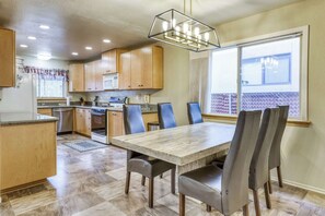 A kitchen with wooden cabinets, a dining table with chairs, a built-in oven, and a window with blinds. - Tahoe Town & Lake Retreat - Near Tahoe Keys (South Lake Tahoe)