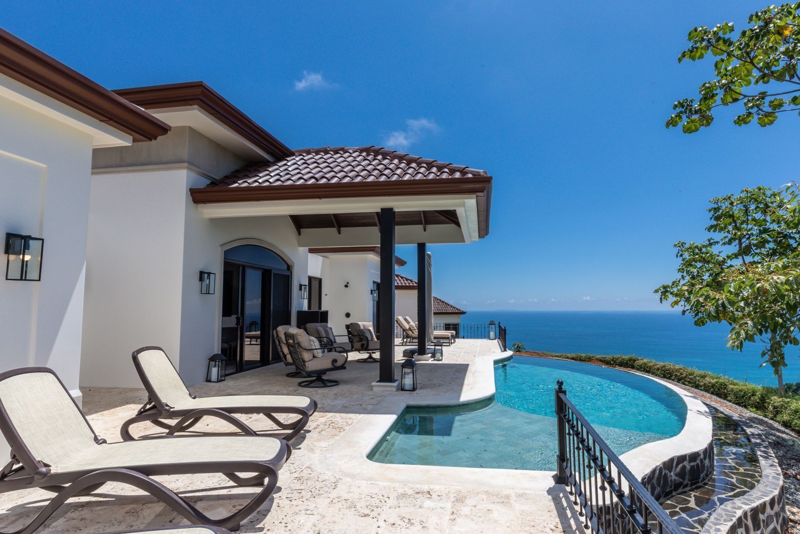 A poolside area with lounge chairs, a pergola, and a view of the ocean.