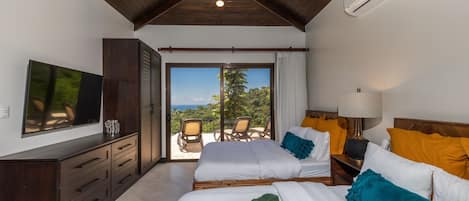Een slaapkamer met een groot bed, een televisie, een kledingkast en een balkon met uitzicht op de oceaan.
