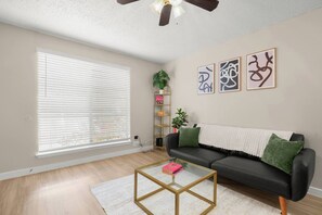 A living room with a black leather sofa, a glass coffee table, a white throw blanket, and abstract wall art. - Austin Medical Hub | Cozy 1BR | Free Parking (Austin)
