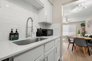 A modern kitchen with a stainless steel sink, a coffee maker, and a microwave. There is a dining area with a table and chairs. - Austin Medical Hub | Cozy 1BR | Free Parking (Austin)