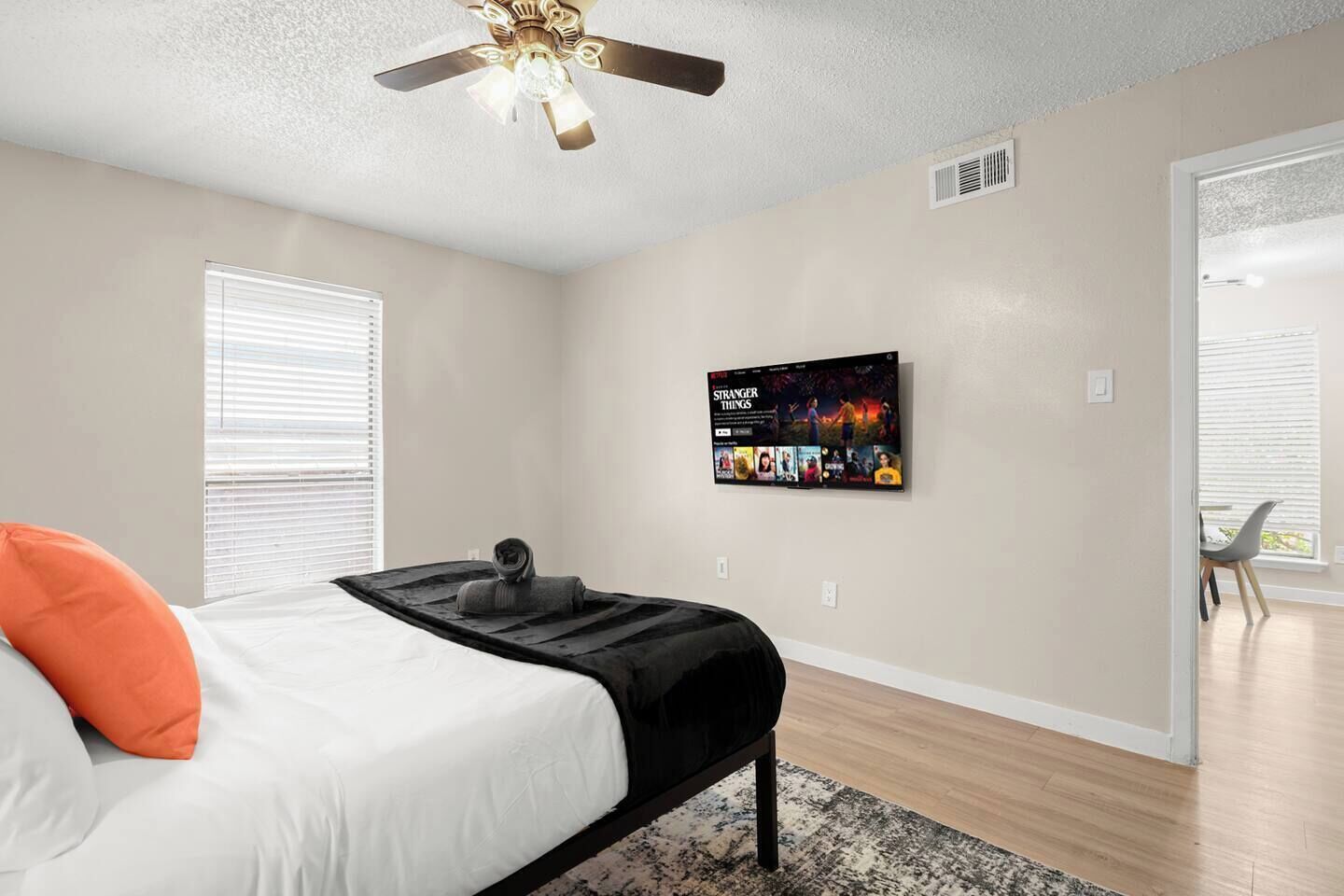 A bedroom with a bed, a ceiling fan, a TV mounted on the wall, and a window with blinds.