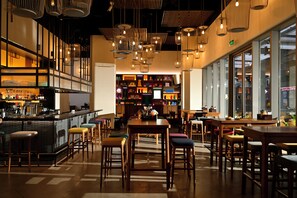 Un espace bar moderne, doté de mobilier en bois, de luminaires suspendus et d’un comptoir.