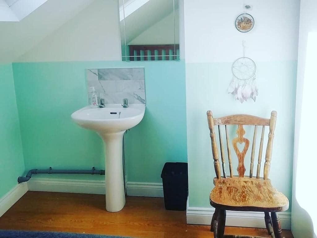Een badkamer met een wastafel op voetstuk, een dromenvanger en een houten stoel.