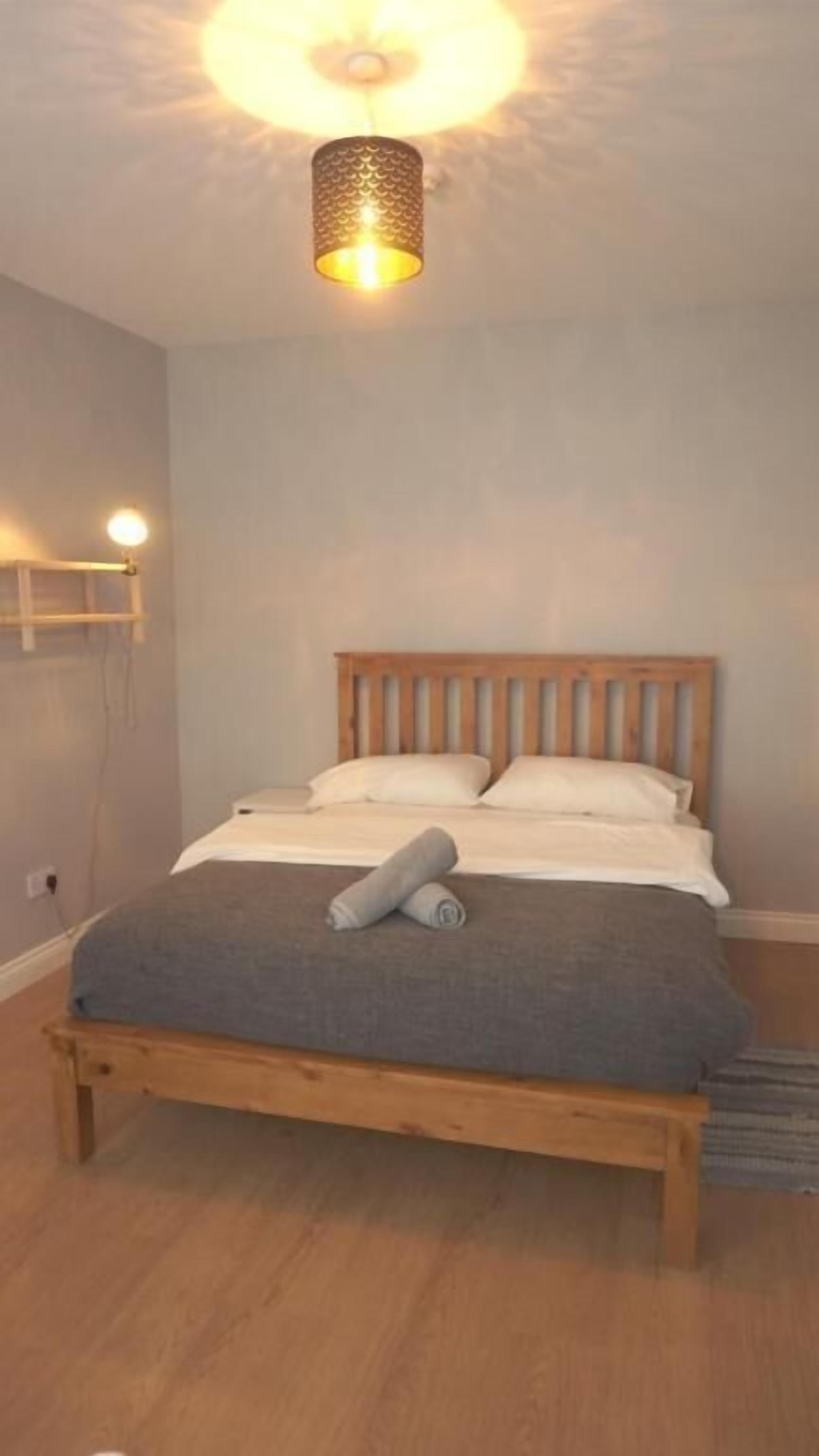 A bedroom with a wooden bed, a bedside lamp, and a wall-mounted light fixture.