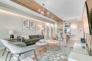 A modern living room with a sofa, armchairs, a coffee table, and a dining area with chairs and a table. - Lake View 3BR/2BA • Themed Rooms SL31418 (Kissimmee)