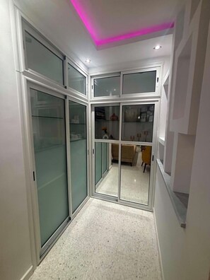 A hallway with a glass partition leading to a room with a bed and a chair.