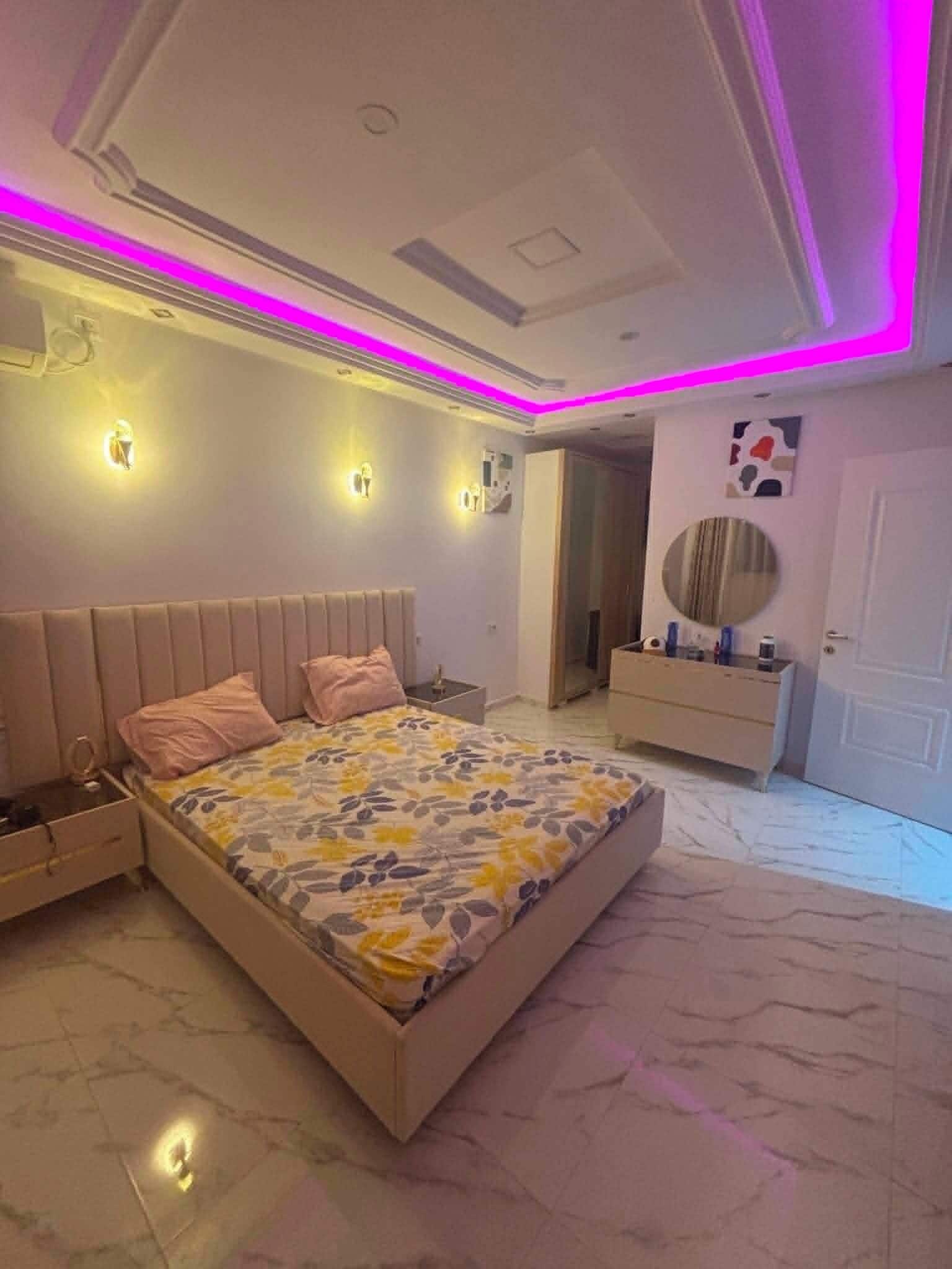 A bedroom with a bed, bedside tables, a vanity, and a mirror.