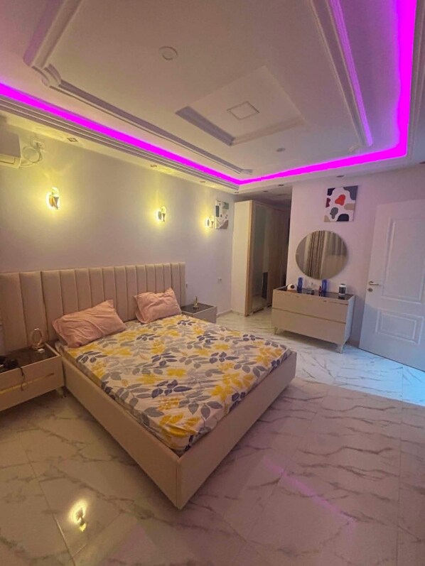 A bedroom with a bed, bedside tables, a vanity, and a mirror.