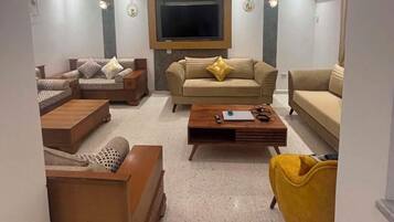 A modern living room with a flat-screen TV, two sofas, a coffee table, and a yellow armchair.