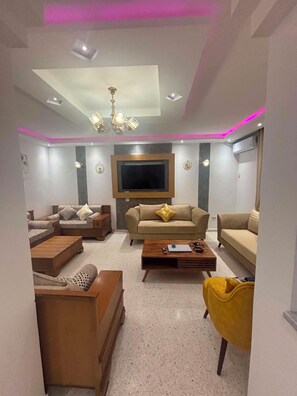 A modern living room with a flat-screen TV, two sofas, a coffee table, and a yellow armchair.