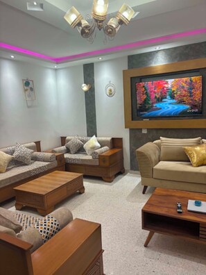 A modern living room with a flat-screen TV mounted on the wall, a sofa set, a coffee table, and a decorative floor lamp.