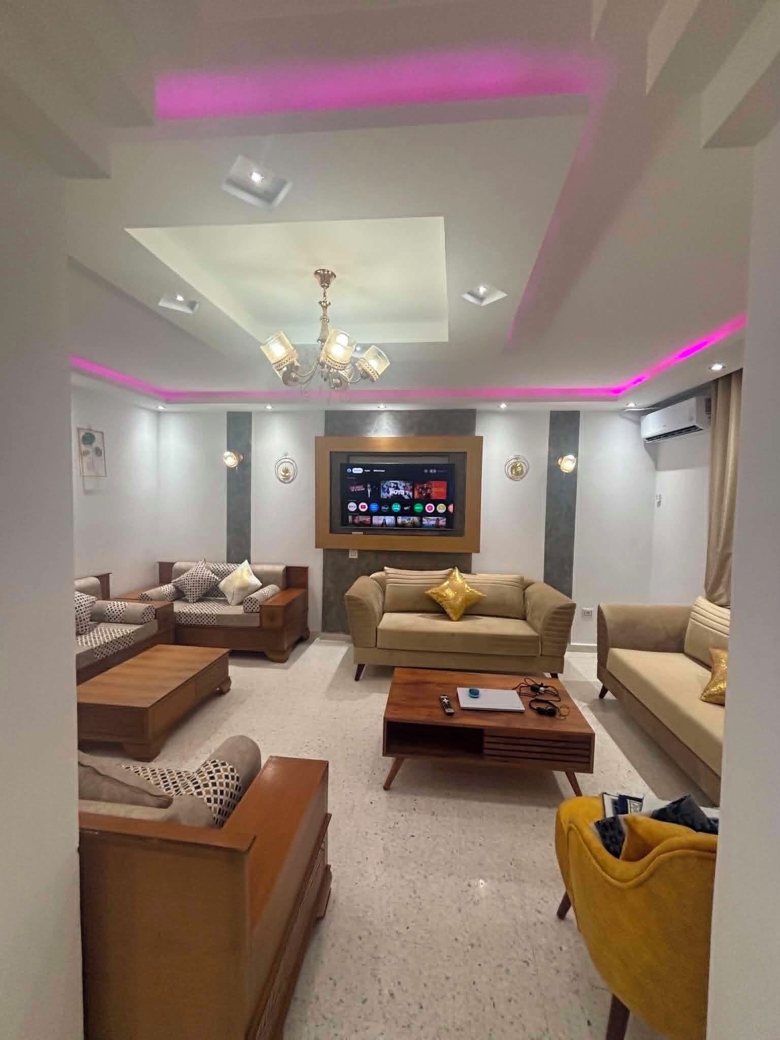 Ein modernes Wohnzimmer mit Flachbildfernseher, Sofas, einem Couchtisch und einer Chandelüster.