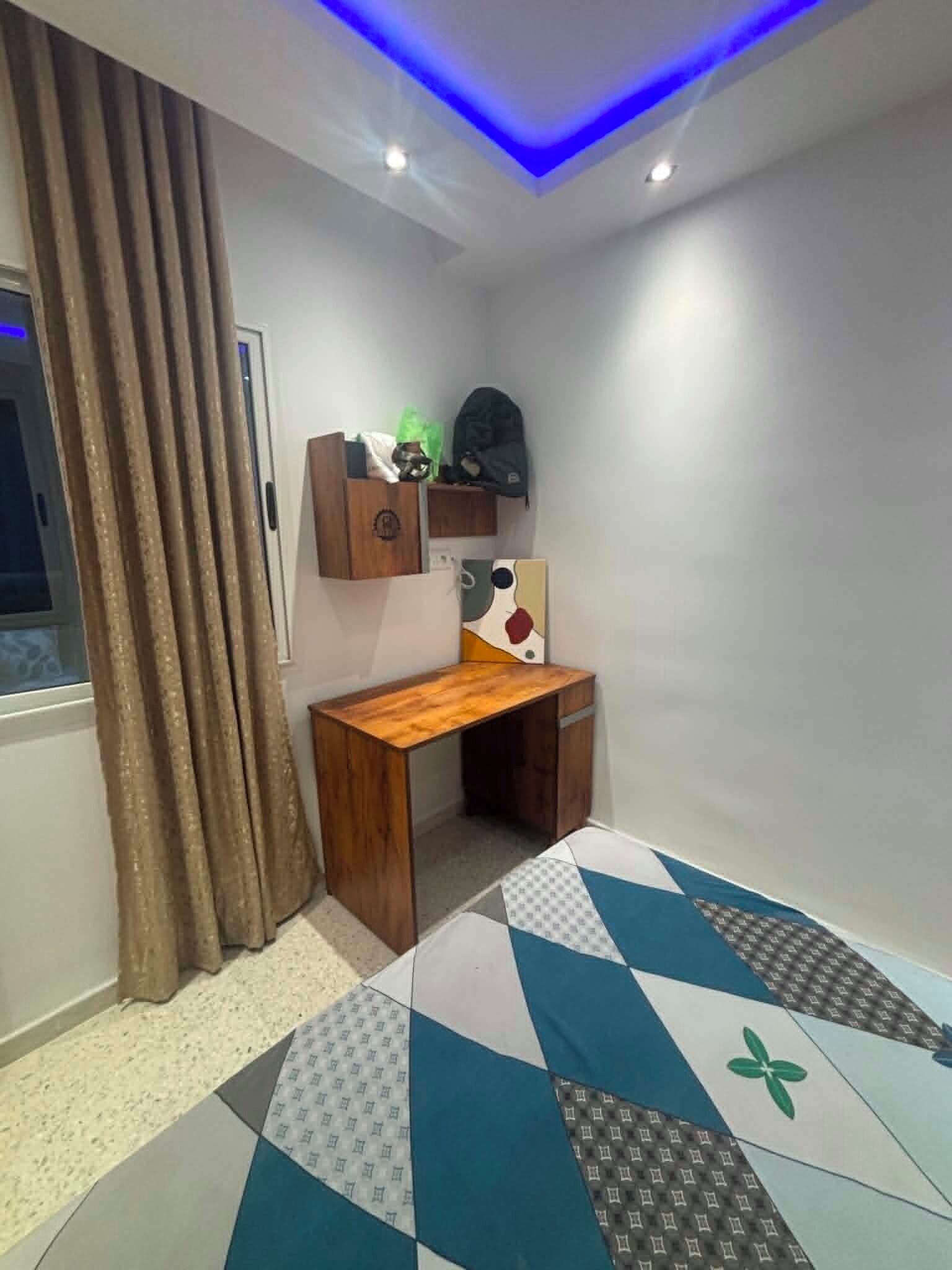 Un dormitorio con cama, escritorio, ventana con cortinas e iluminación en el techo.
