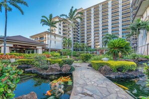 Resort com lago de carpas, palmeiras e um prédio grande com várias varandas.