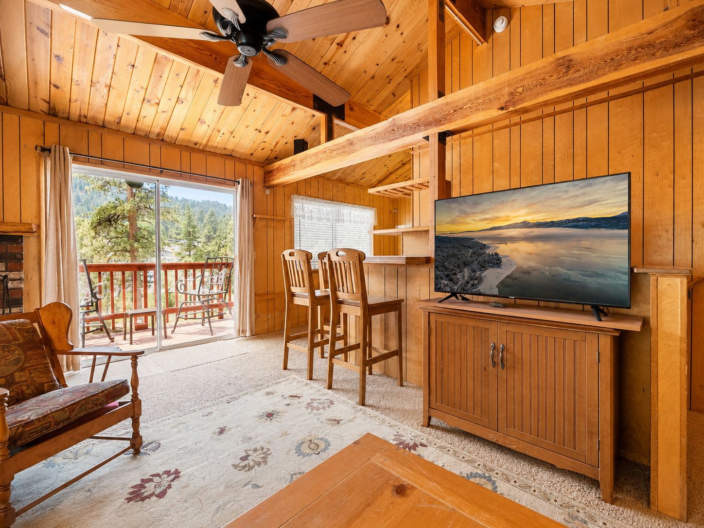 Un interior de madera con un ventilador de techo, un televisor sobre un mueble de madera, un sofá y una zona de comedor con sillas.