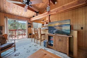 A wooden interior with a television, seating area, and a view through a glass door. - The Moonridge Escape (Big Bear Lake)