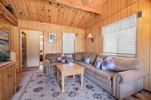 A cozy cabin interior with a wooden ceiling, a sofa set, a television on a cabinet, and a patterned rug. - The Moonridge Escape (Big Bear Lake)